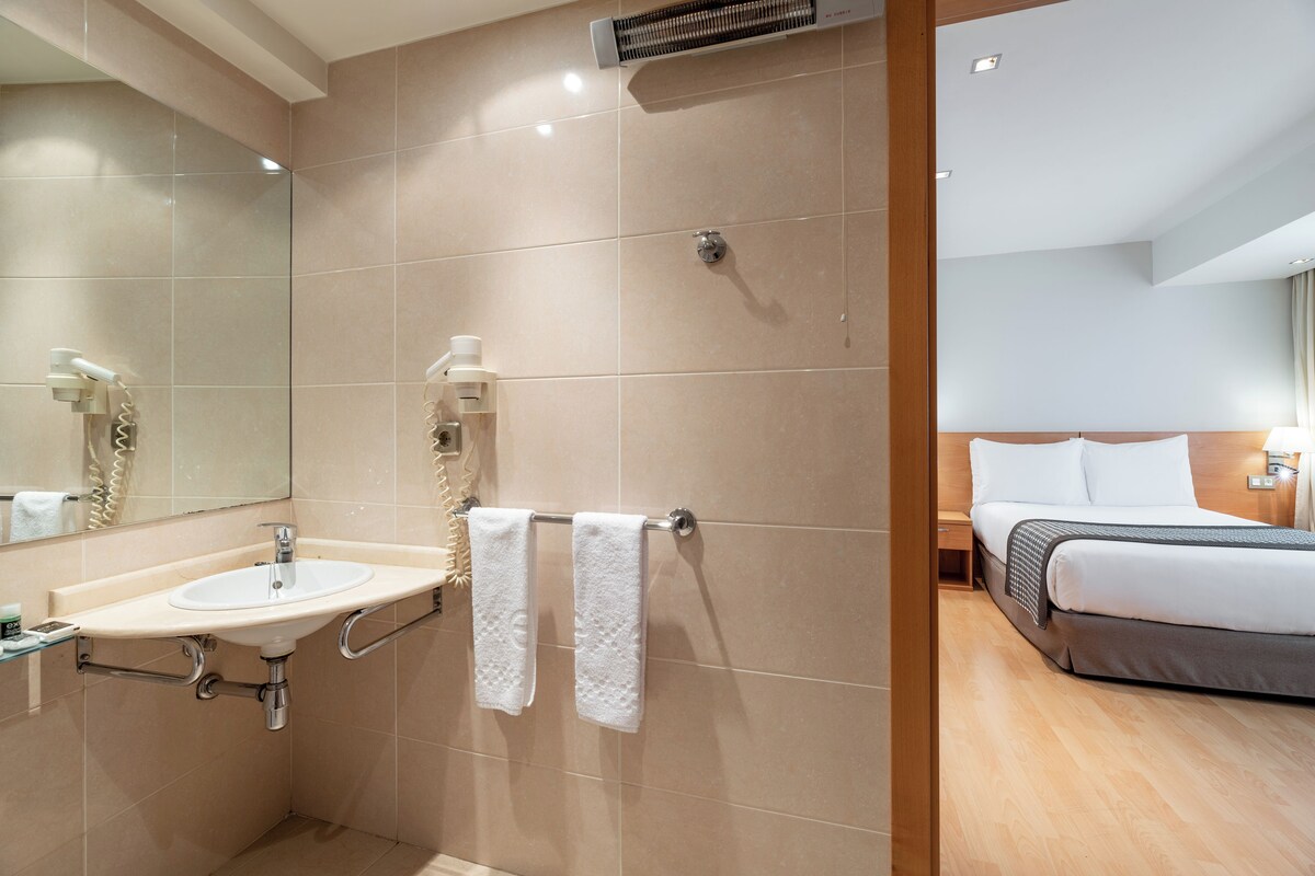 A hotel bathroom with a sink, mirror, towel rack, and a shower area.