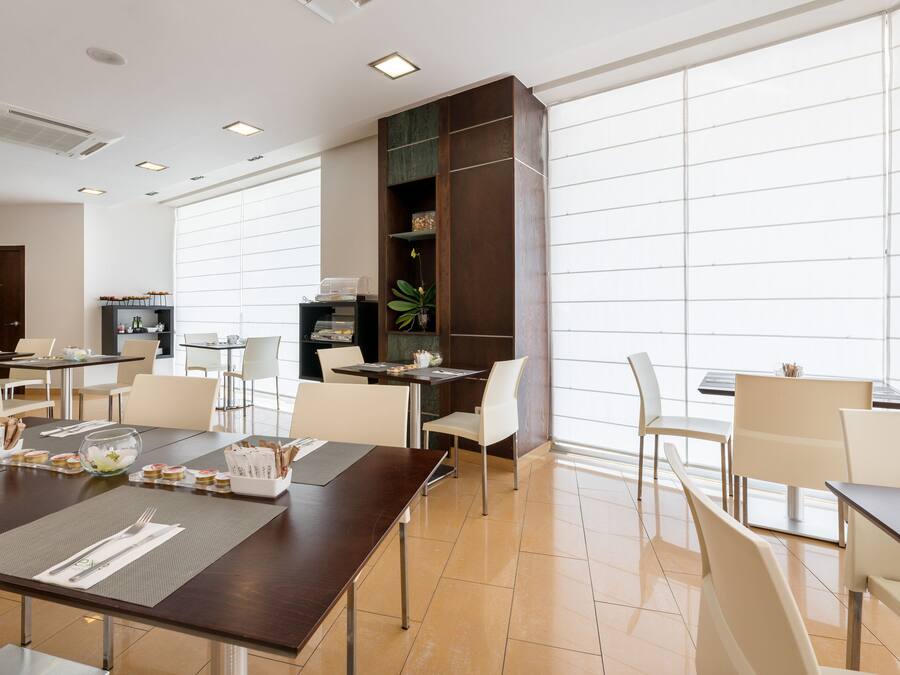 Un comedor moderno con mesas y sillas, un amplio ventanal y una estantería decorativa con plantas.
