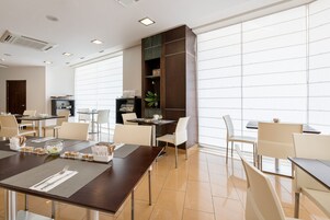 Un comedor moderno con mesas y sillas, un amplio ventanal y una estantería decorativa con plantas.