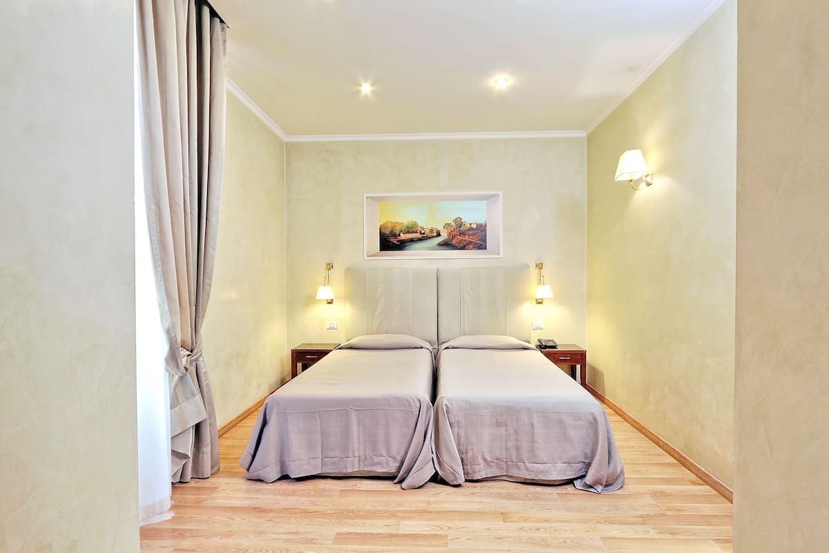 A room with two beds, a painting on the wall, and two bedside lamps.