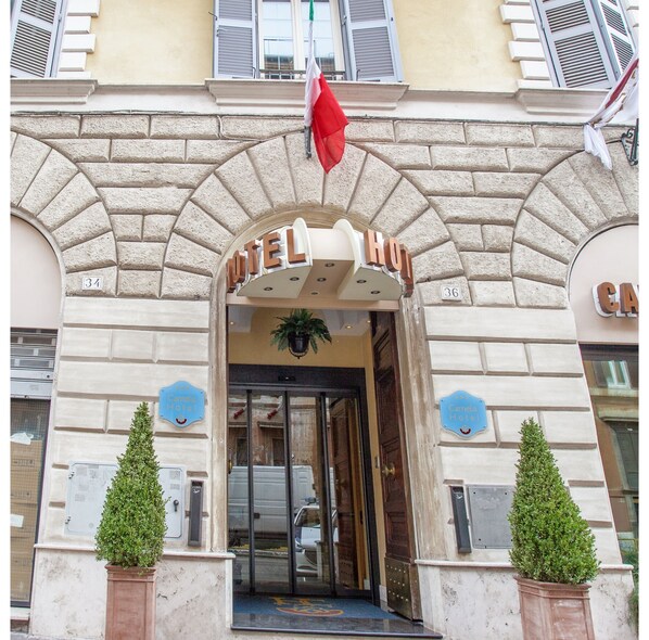 L’entrée d’un hôtel, avec une façade en pierre, un drapeau et deux plantes en pot.