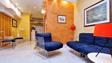 A modern lobby with marble flooring, blue sofas, a red lamp, and framed artwork on the walls.
