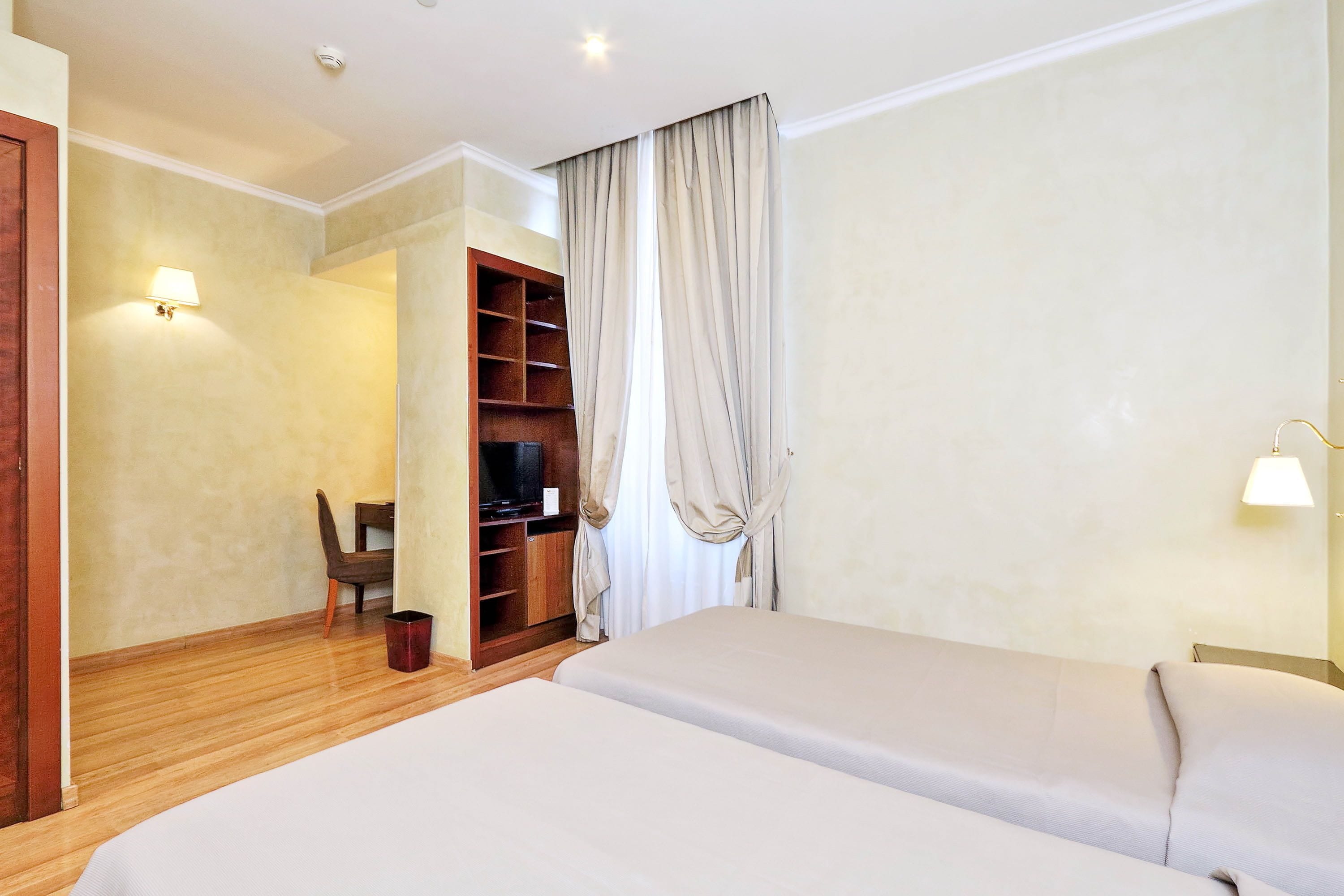 Habitación de hotel con dos camas, un escritorio, una silla y un armario.