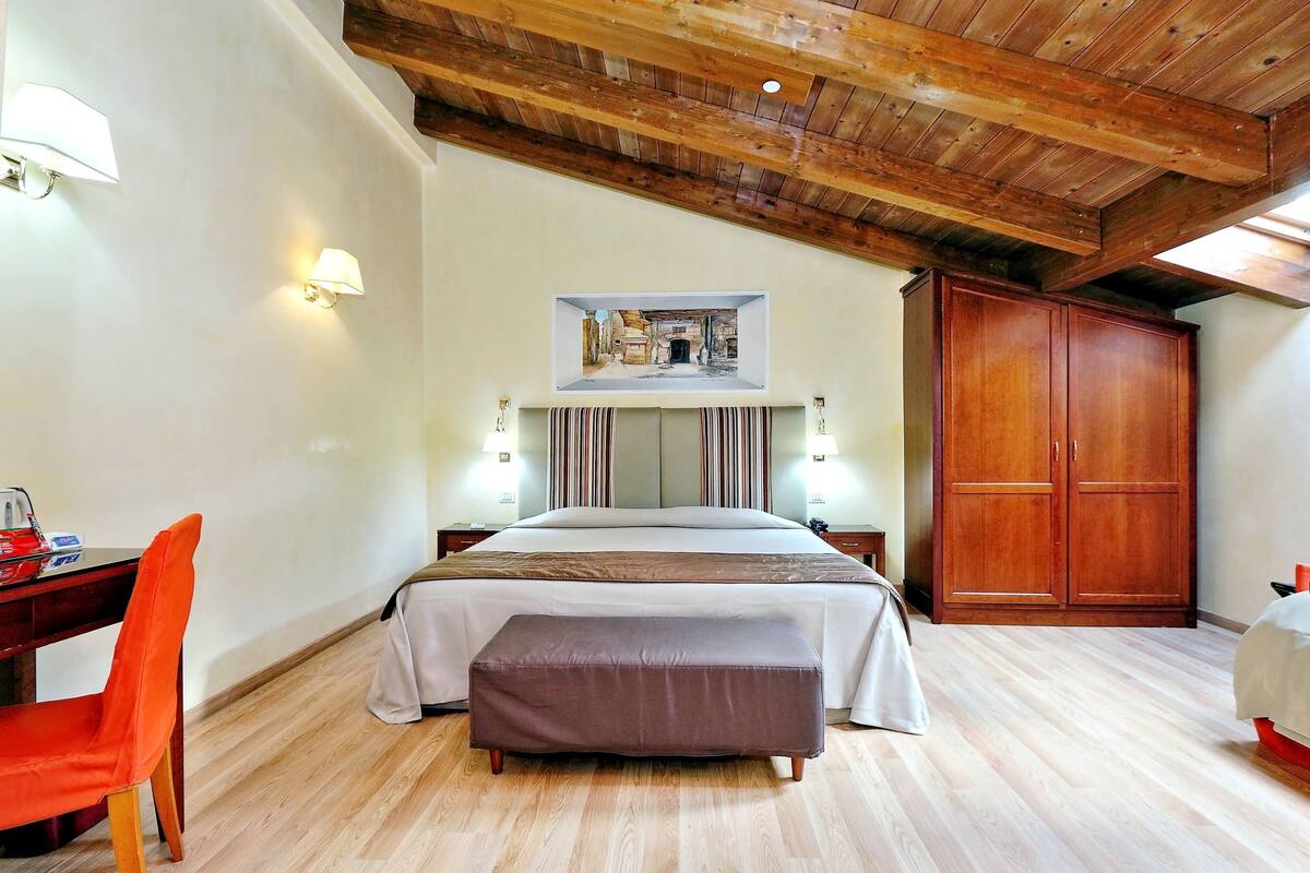 A bedroom with a wooden ceiling, a bed with a headboard, a desk with a chair, and a wardrobe.