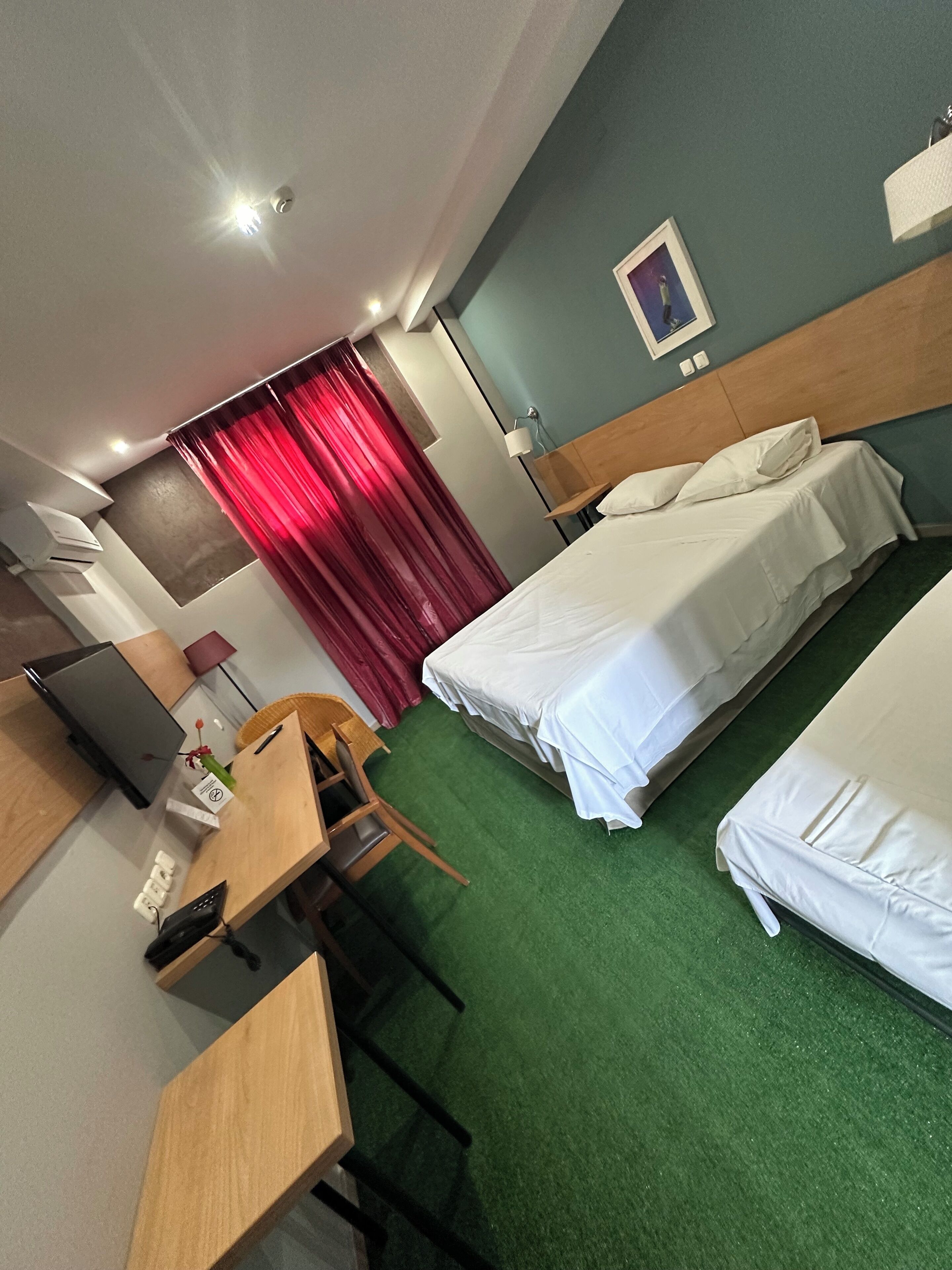 Ein Hotelzimmer mit zwei Betten, einem Schreibtisch, einem Stuhl, einem Fernseher und einem roten Vorhang.