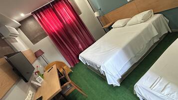 Ein Hotelzimmer mit zwei Betten, einem Schreibtisch, einem Stuhl, einem Fernseher und einem roten Vorhang.
