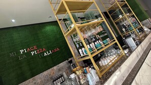 Un espace d’accueil agrémenté d’un mur végétal et d’une enseigne indiquant : « MI PLACE LA PIZZA ITALIANA ». On y trouve deux étagères dorées où sont exposés divers articles, notamment des bouteilles et des objets en verre.