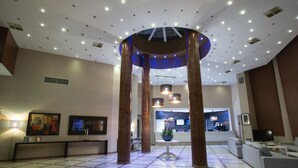 Un hall d’entrée spacieux avec une colonne centrale, un comptoir d’accueil et un espace détente.