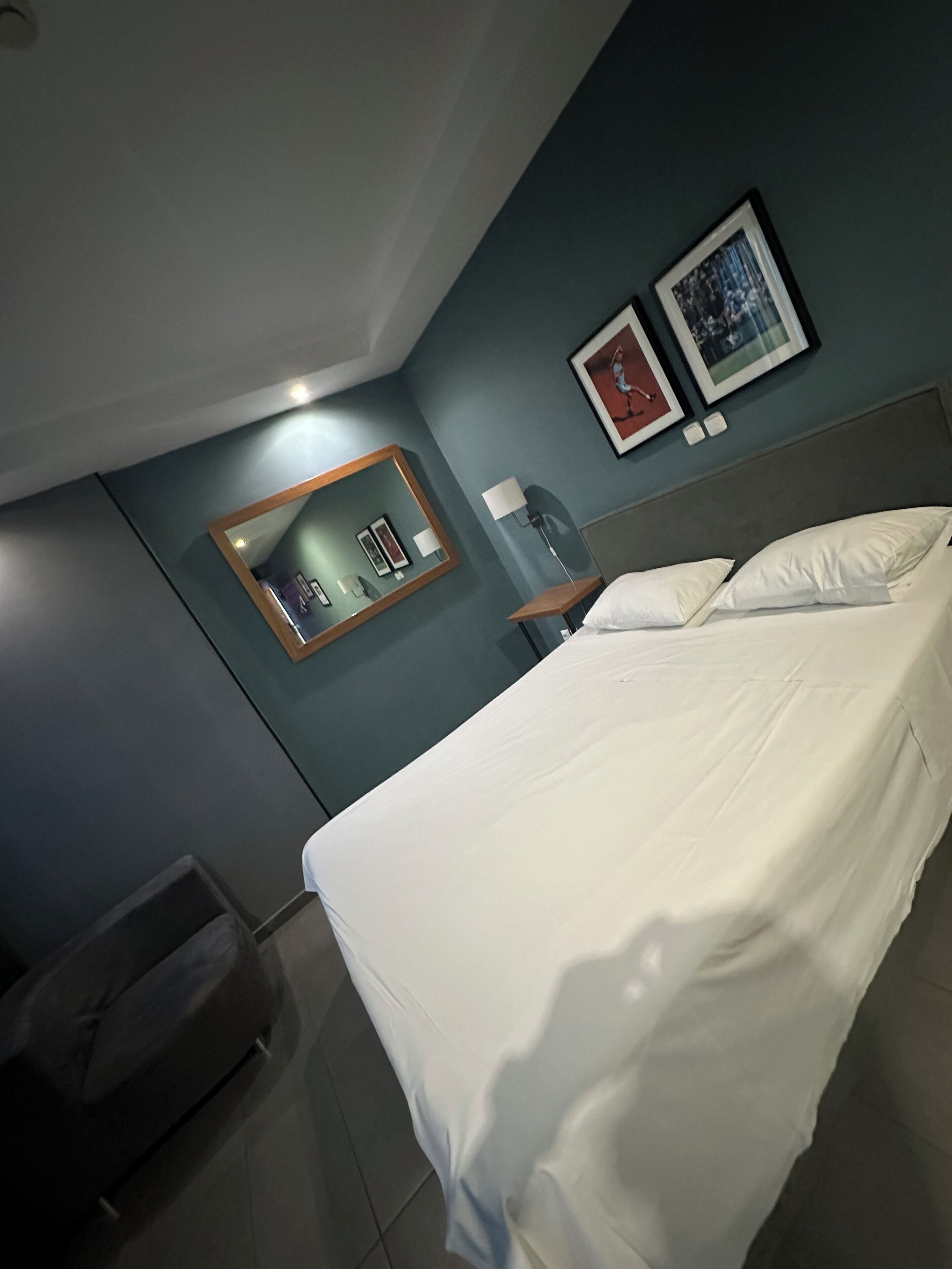 Ett hotellrum med en säng, ett sängbord, en spegel och två inramade tavlor på väggen.