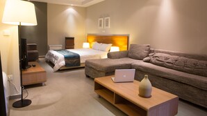 Une chambre d’hôtel moderne équipée d’un lit, d’un canapé, d’un bureau avec un ordinateur portable, d’une lampe et d’une télévision.