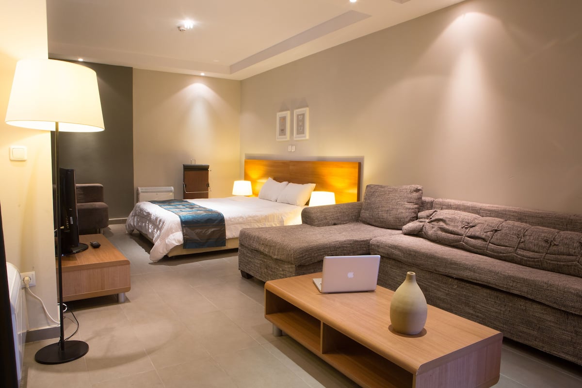 Een moderne hotelkamer met een bed, een bank, een bureau met een laptop, een lamp en een televisie.