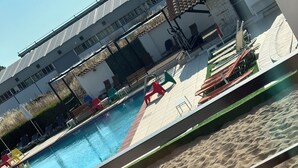 Une piscine avec une zone de plage de sable, des chaises longues et un espace de repos couvert.