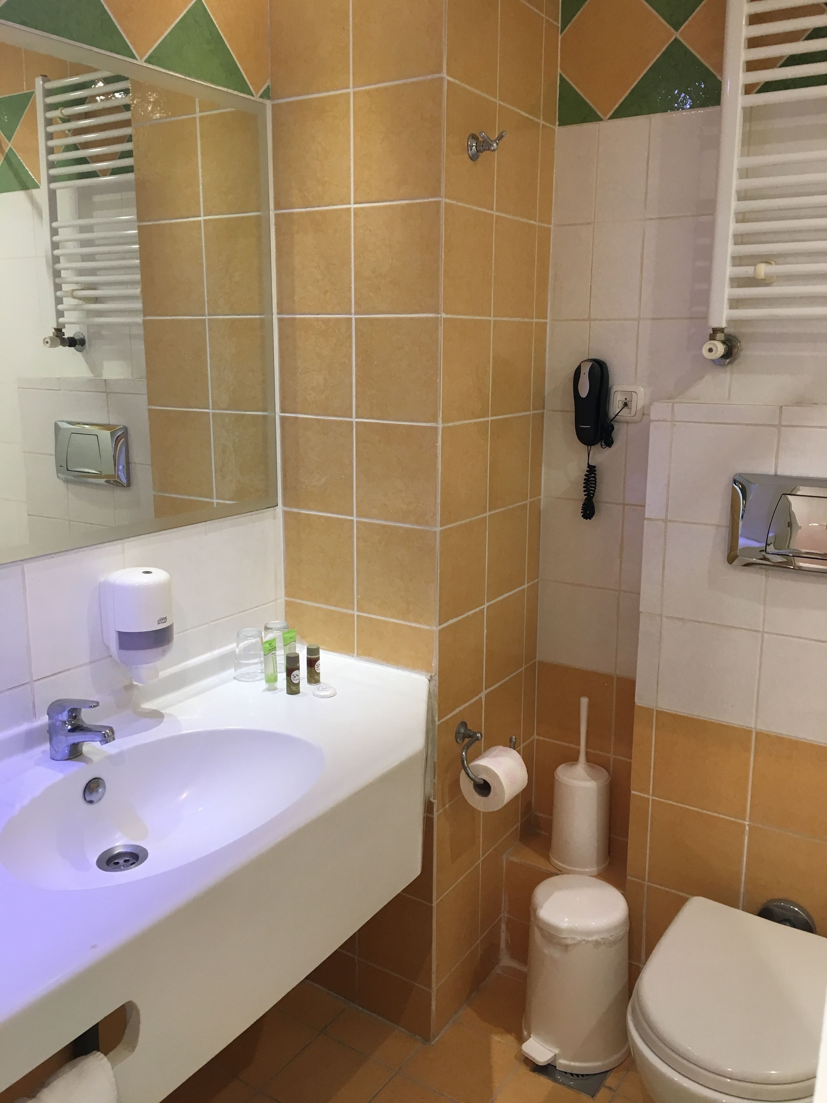 A bathroom with a sink, mirror, toilet, and a hand dryer.