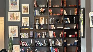 A living room with a large bookshelf filled with books and decorative items, a coffee table with books and a vase, and a patterned rug.