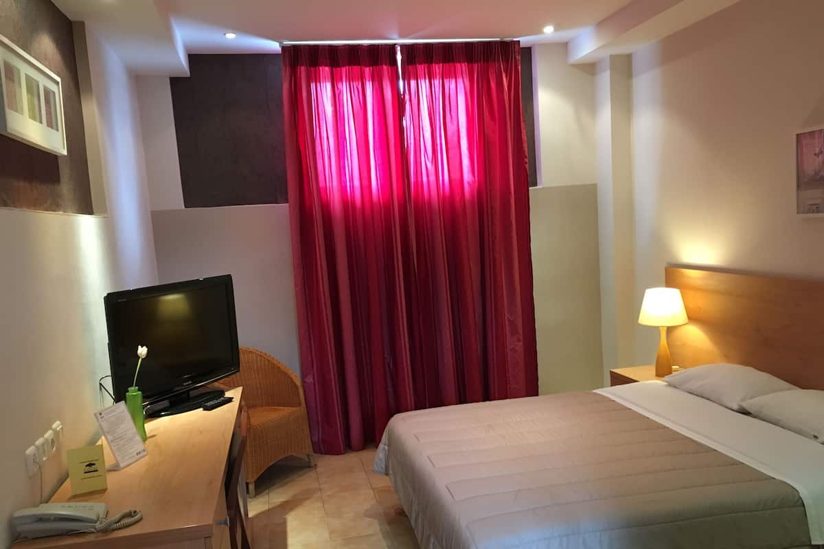 Een hotelkamer met een bed, een bureau met een televisie, een telefoon en een lamp.