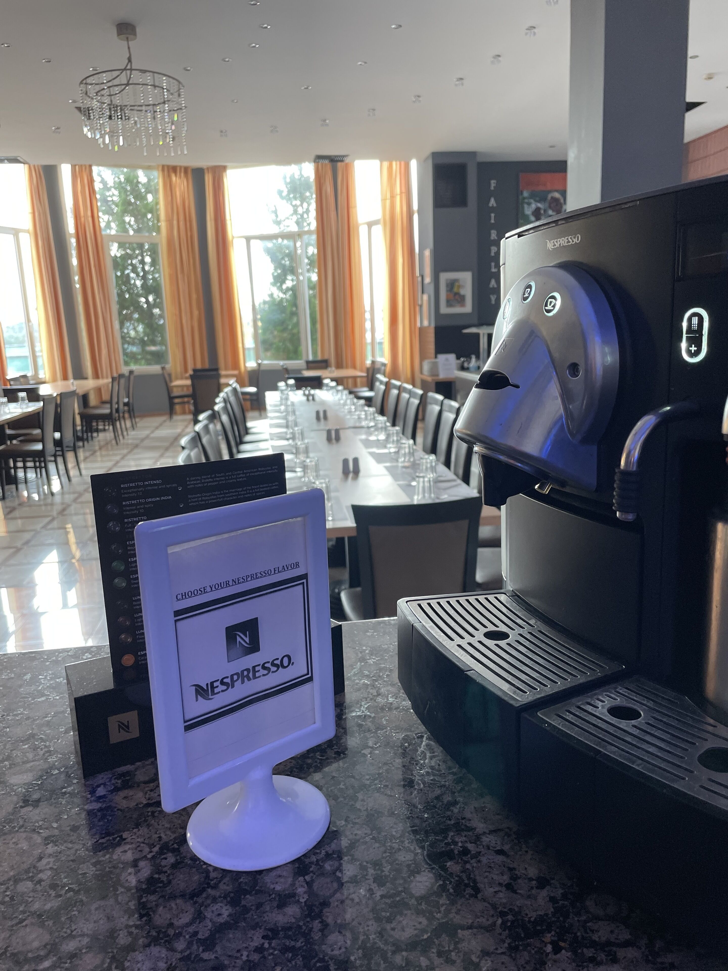 A modern dining area with a long table set for a meal, a Nespresso coffee machine, and a menu stand.