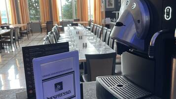 Ein moderner Essbereich mit einem langen Tisch, gedeckt für eine Mahlzeit, einer Nespresso-Kaffeemaschine und einem Menüständer.