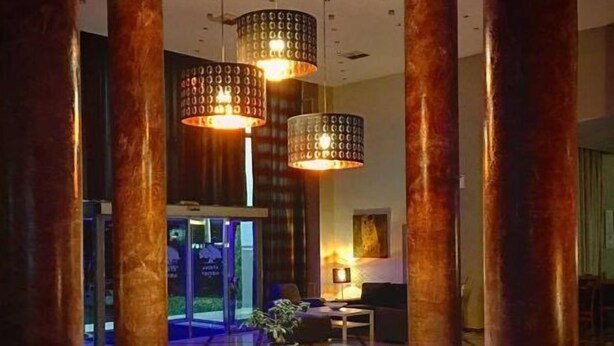 Un hall d’entrée doté de grandes colonnes, une table ronde centrale agrémentée d’une plante et un éclairage moderne.
