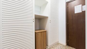 Un couloir avec une armoire en bois, une porte-penderie blanche dotée de stores horizontaux et une porte en bois sur laquelle est affiché un avis.