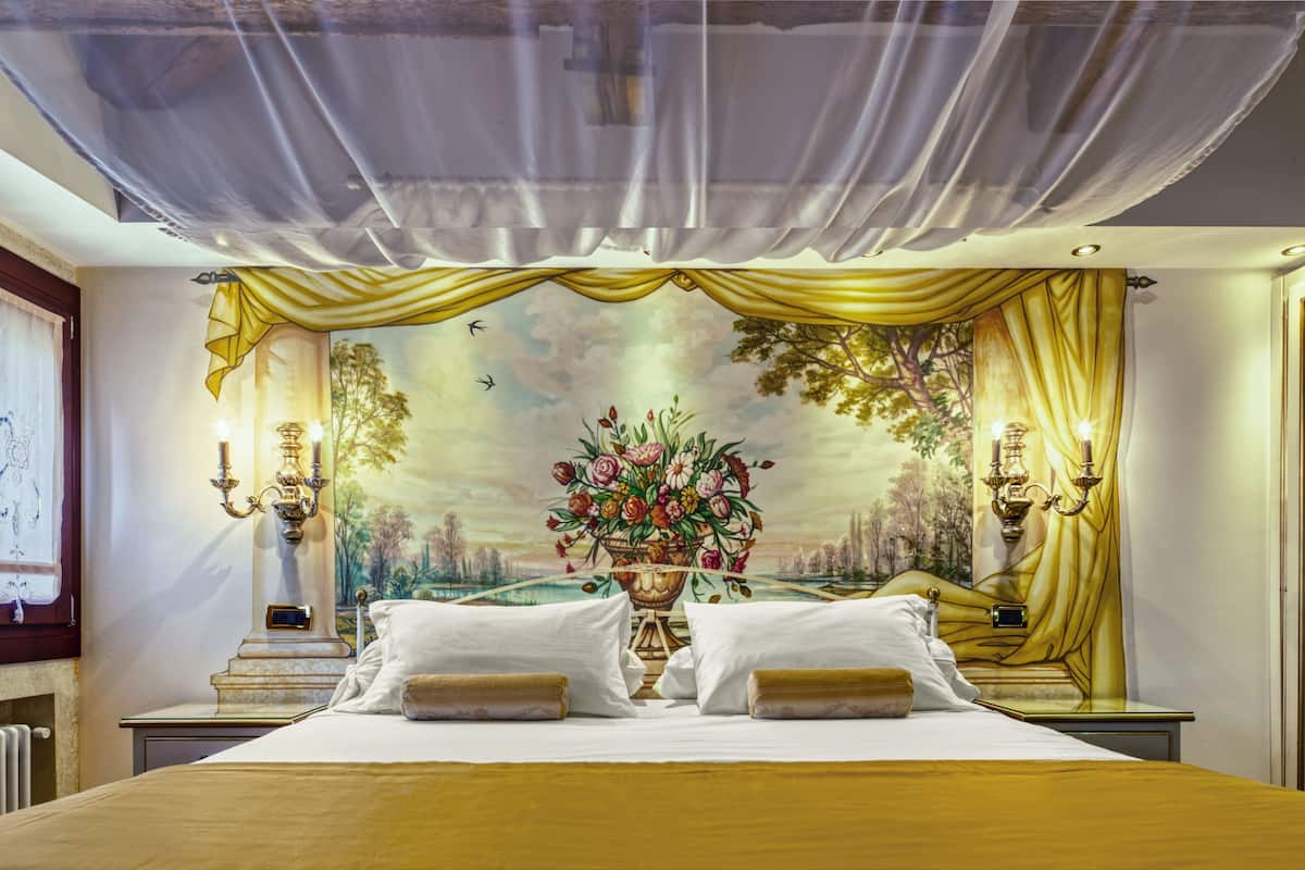 A hotel room with a large bed, a chandelier, and a mural on the wall.