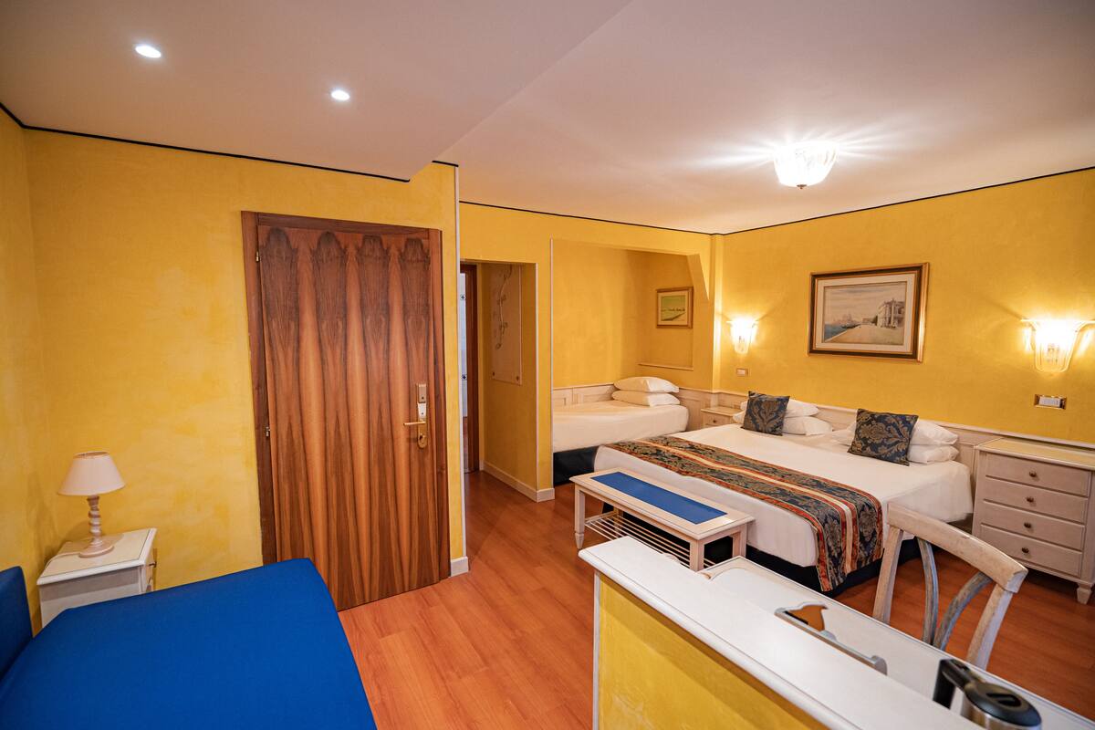 A hotel room with a bed, a desk, a chair, a lamp, and a wardrobe.