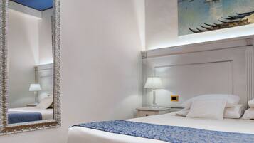 A hotel room with a bed, a nightstand with a lamp, a large mirror, and a painting of boats on the wall.
