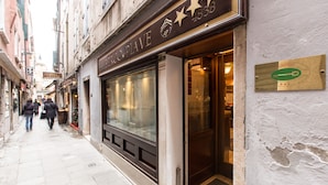 A narrow street with a building featuring a large glass window and a plaque on the wall. - Hotel al Piave (Venice)