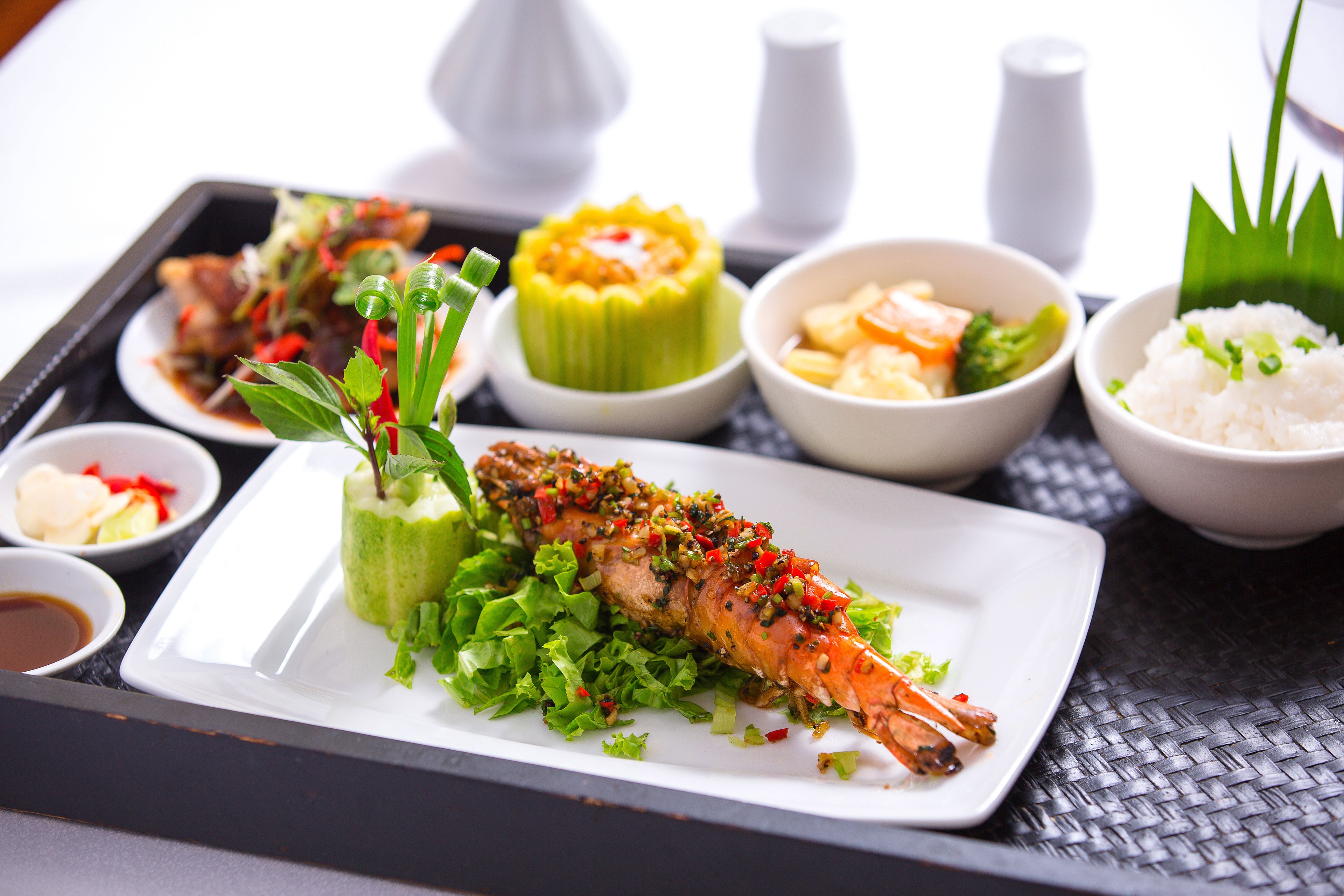 A tray with various dishes including a grilled fish, a green vegetable dish, and bowls of rice and vegetables.
