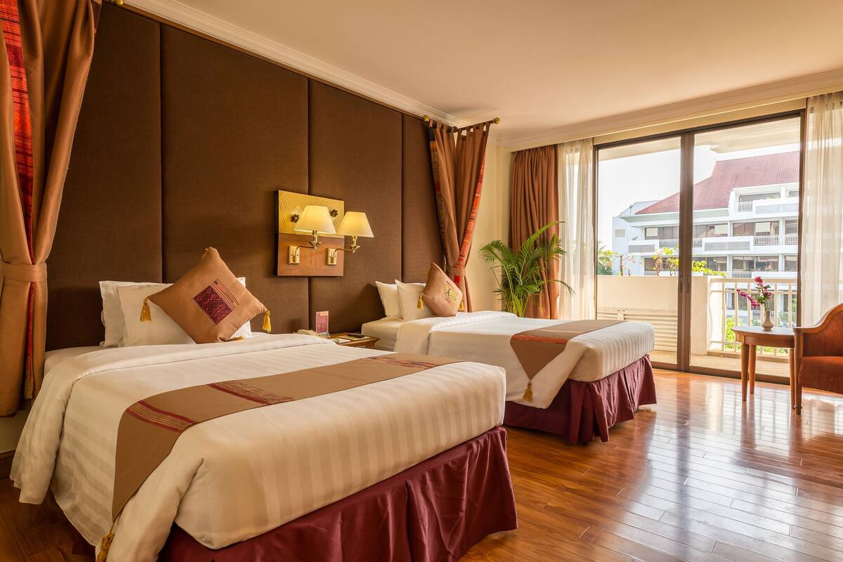 A hotel room with two beds, a balcony, and a view of a building.