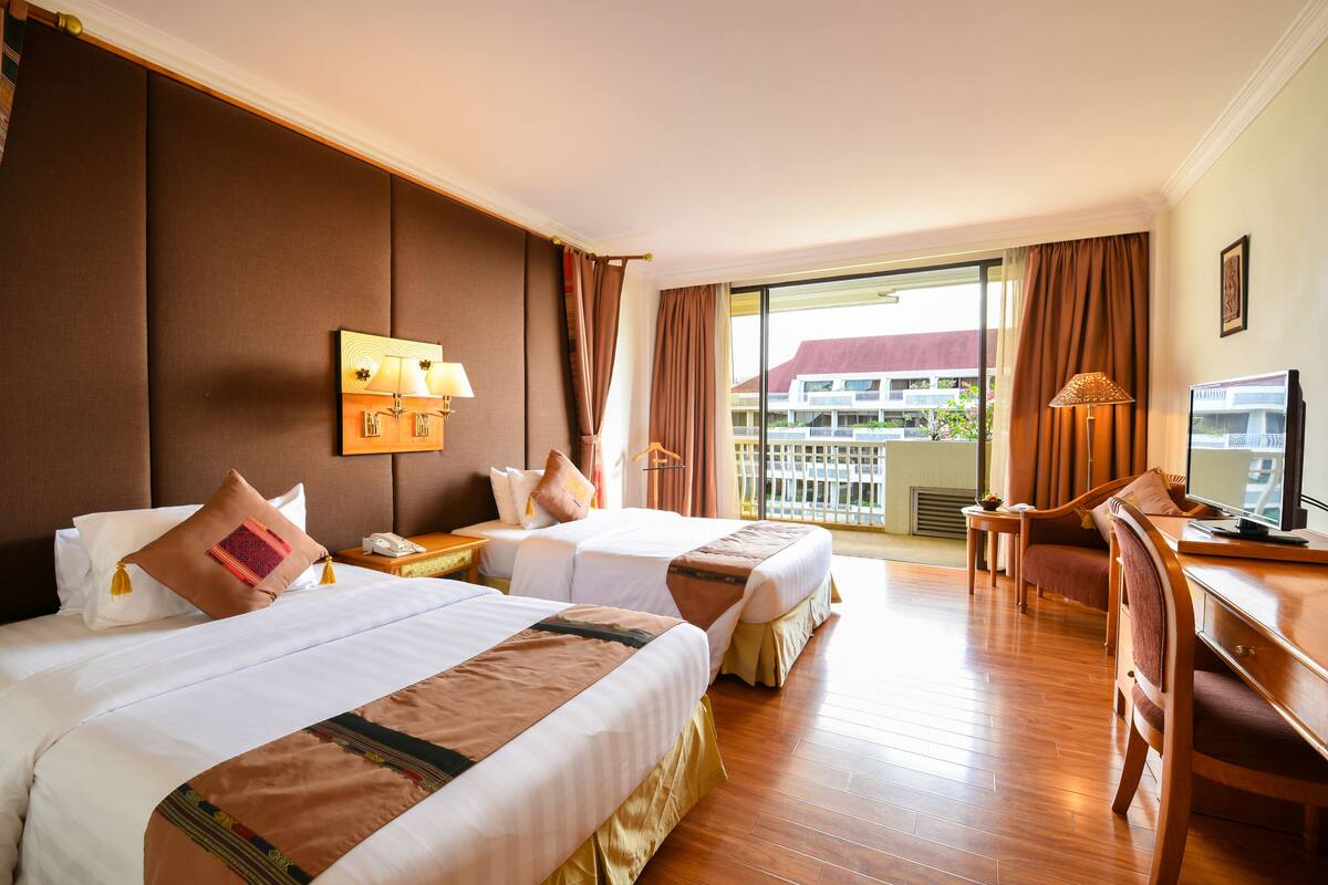 A hotel room with two beds, a desk, a chair, and a television.