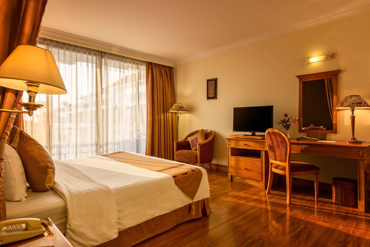 A hotel room with a bed, desk, chair, television, and a window with curtains.