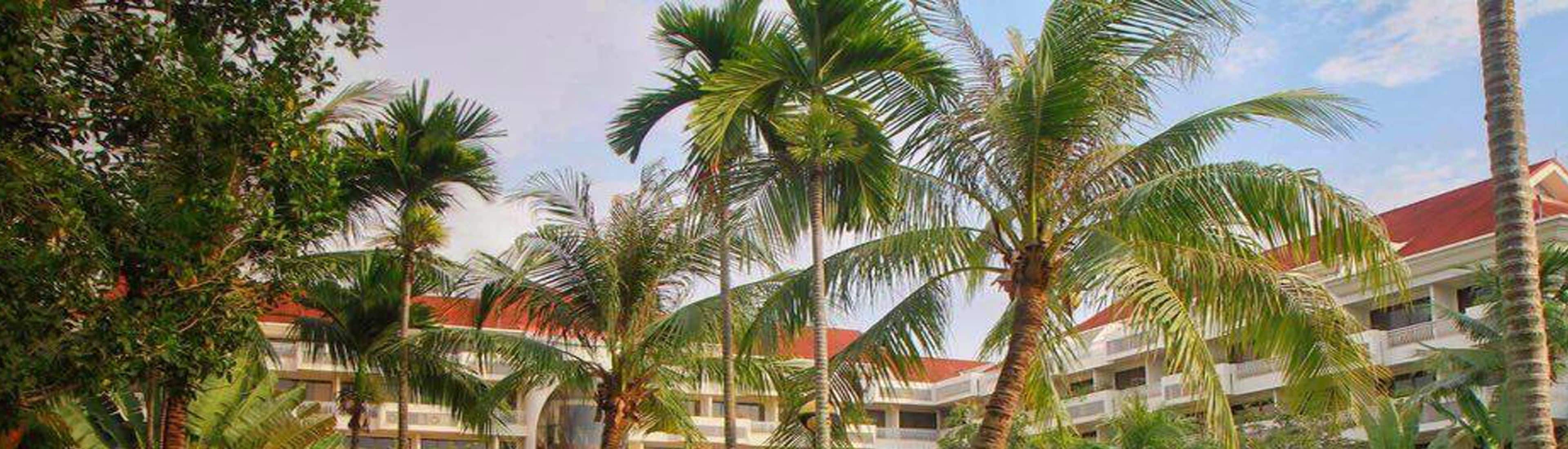 A hotel with multiple floors, palm trees, and a red-roofed building.