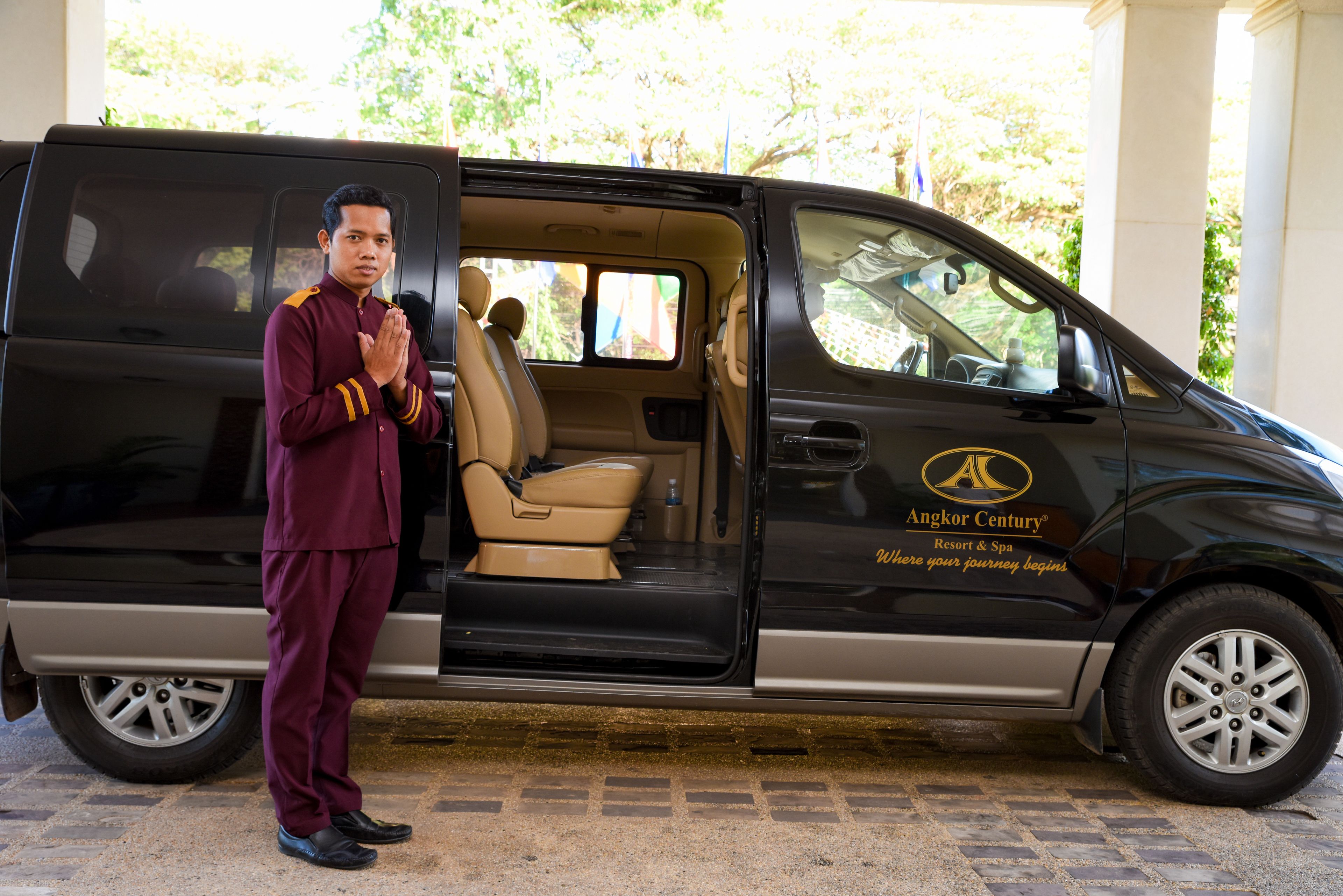 A black van with a beige interior, a logo on the side, and a person standing in front of it.