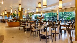 A spacious restaurant with high ceilings, pendant lighting, and a central bar area. Tables are neatly arranged with chairs, and the space is well-lit.
