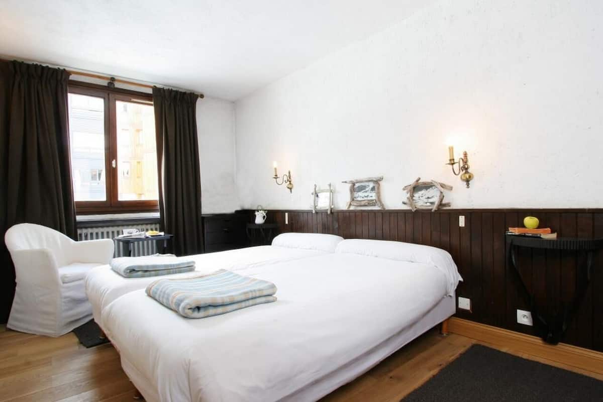 Habitación de hotel con una cama grande, una silla, una mesita y una ventana con cortinas.