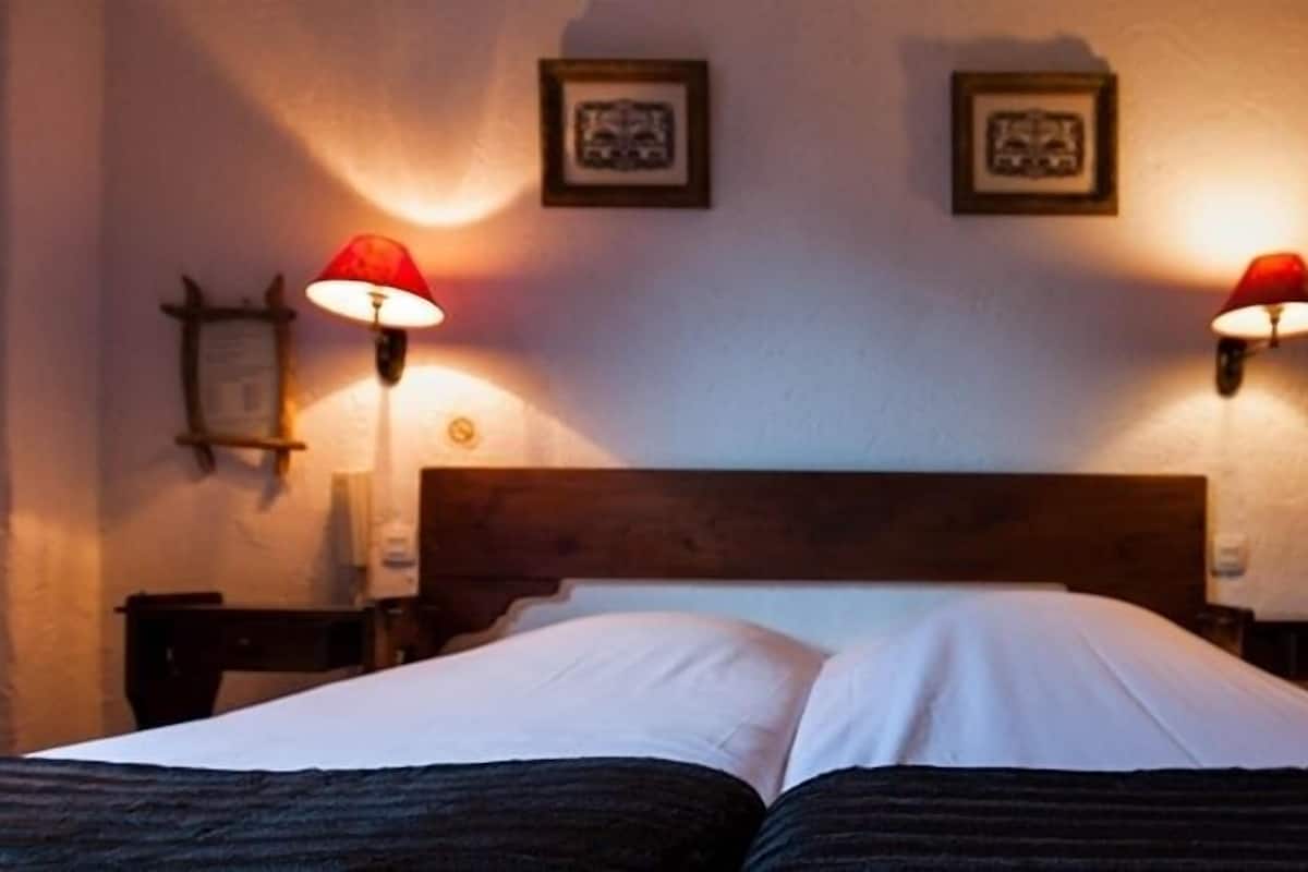 Una cama doble con dos mesitas de noche, cada una con una lámpara roja. Encima de la cama, hay dos cuadros enmarcados en la pared.