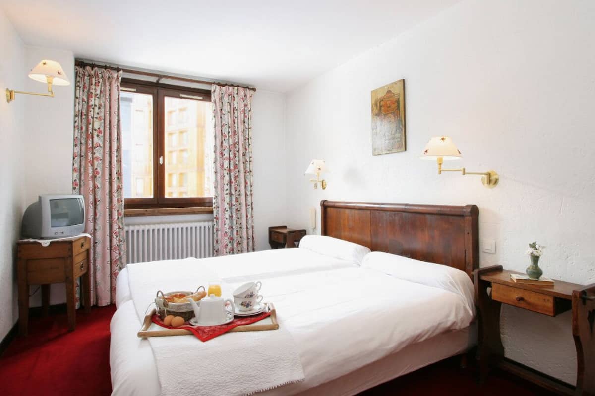Habitación de hotel con cama doble, una mesita de noche pequeña, lámpara de pared y un cuadro.