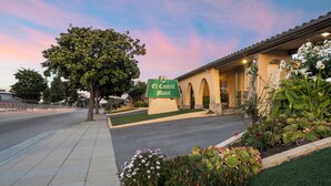 A motel with a sign, a paved driveway, and landscaped areas with various plants. - El Castell Motel (Monterey)