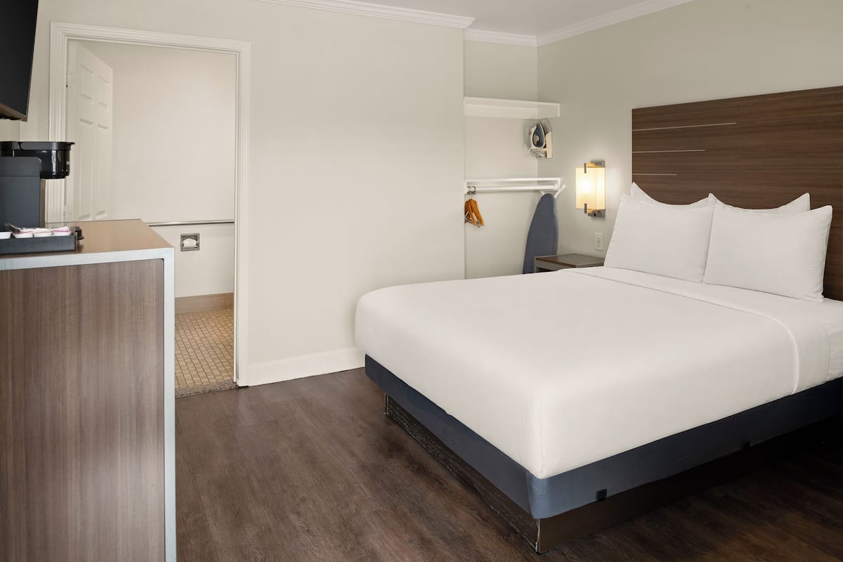 A hotel room with a bed, a desk, a coffee maker, a coat rack, and a wall-mounted ironing board.