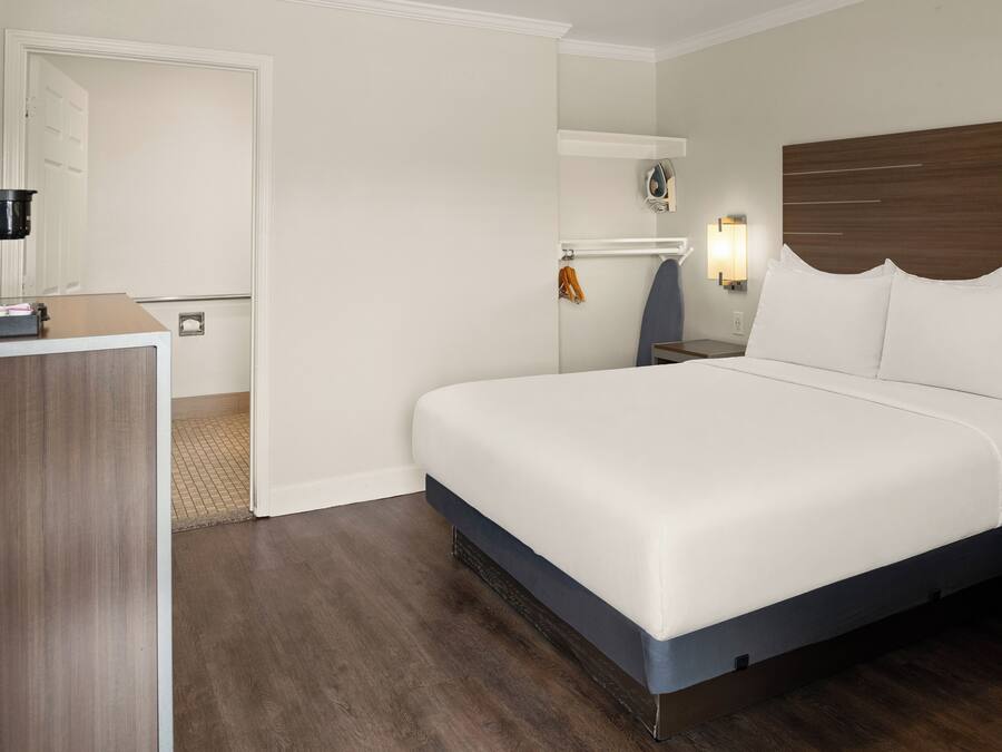A hotel room with a bed, a desk, a coffee maker, a coat rack, and a wall-mounted ironing board.
