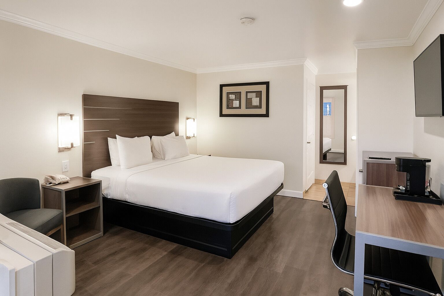 Una habitación de hotel con cama, mesita de noche, silla, escritorio y cafetera.