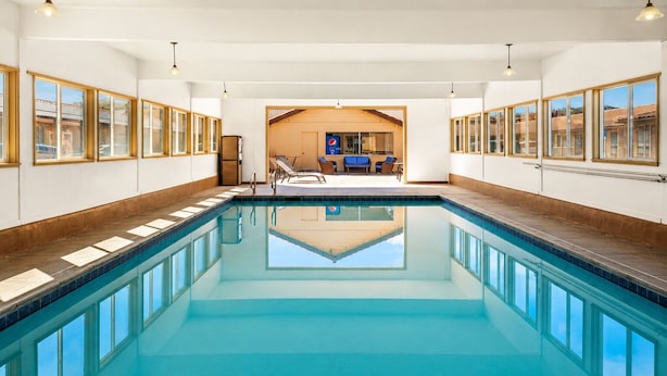 A large indoor swimming pool with clear blue water, wooden deck, and a view of a dining area with tables and chairs. - El Castell Motel (Monterey)
