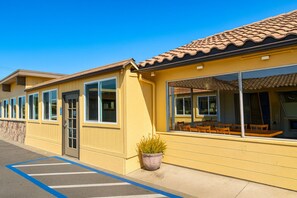 A yellow building with large windows and a patio area with wooden furniture.