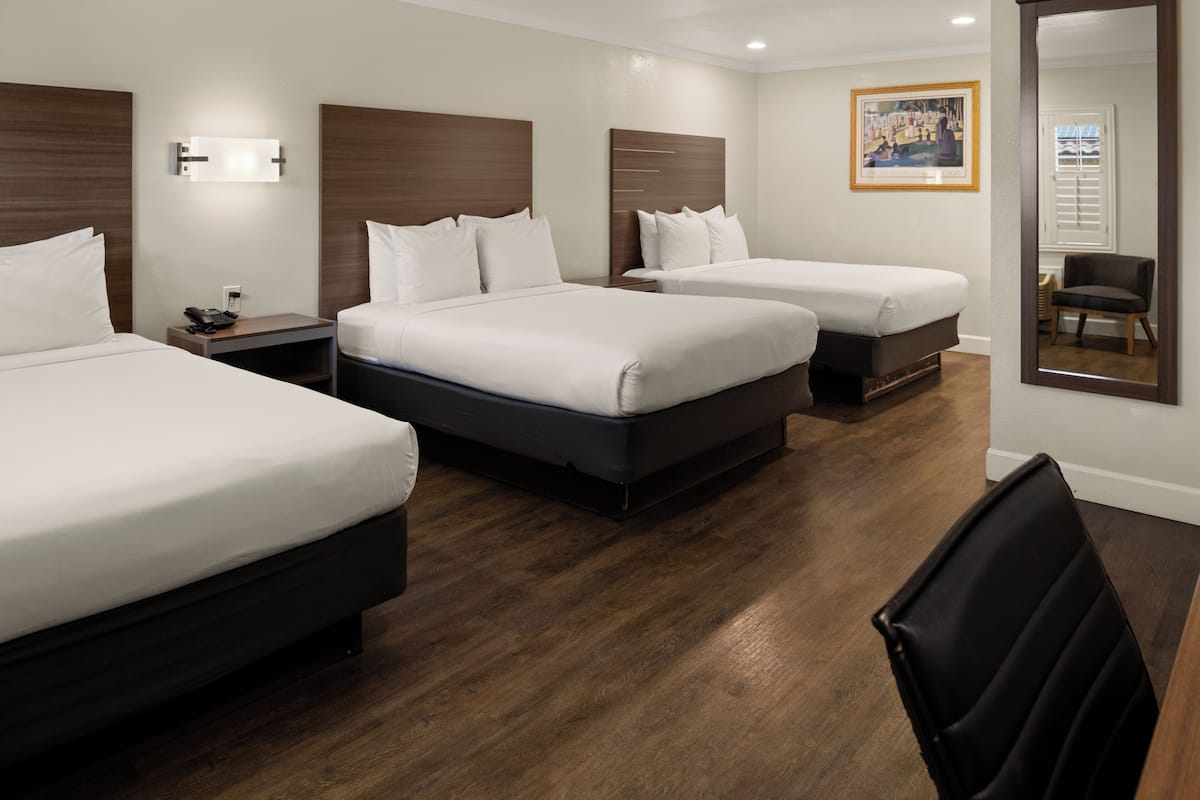 A hotel room with two beds, a desk, a chair, and a large mirror.