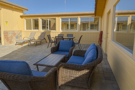 An outdoor patio area with wicker furniture, a table, and a view of a building with large windows.. El Castell Motel