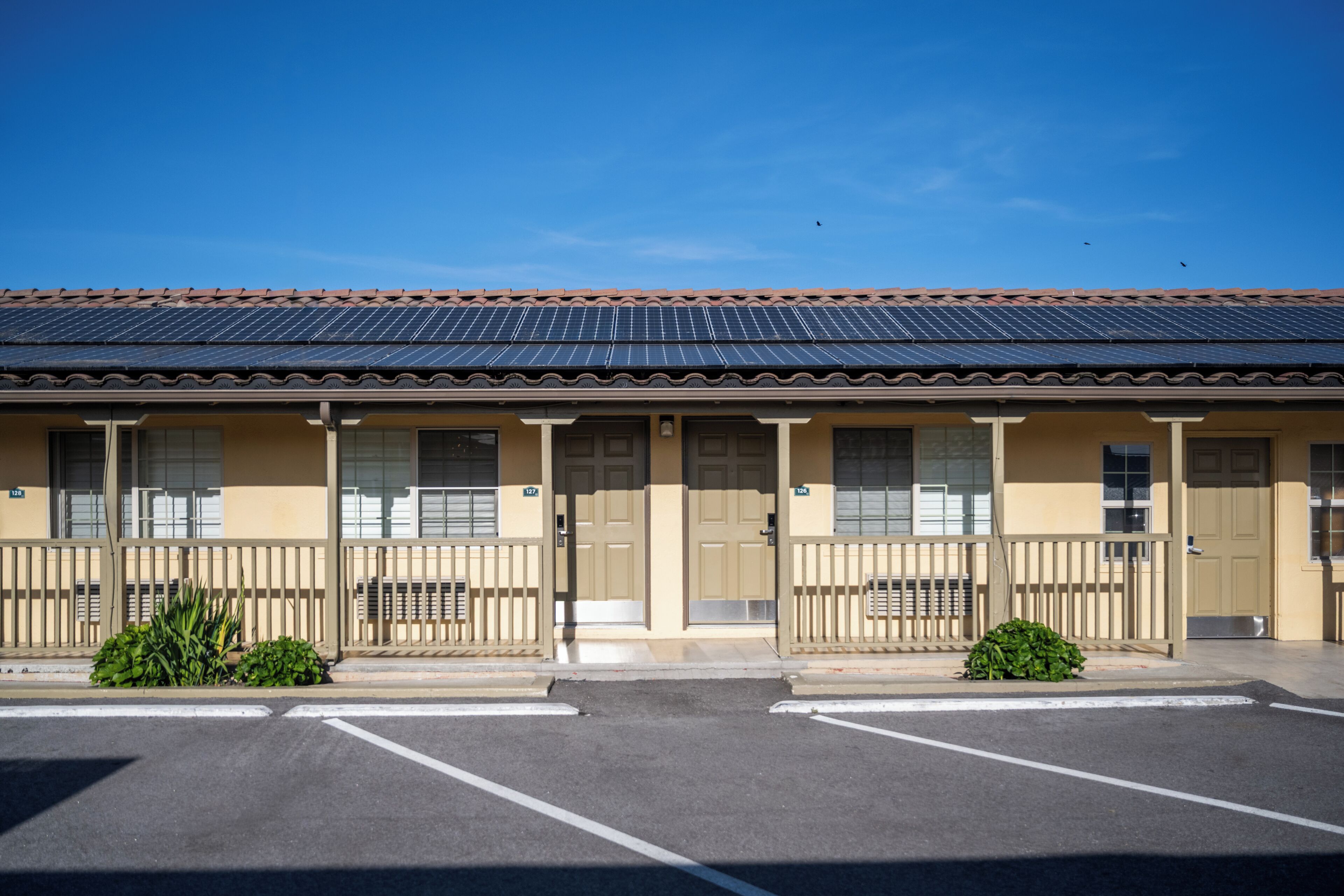 A motel with a tiled roof, multiple doors, and a parking lot.