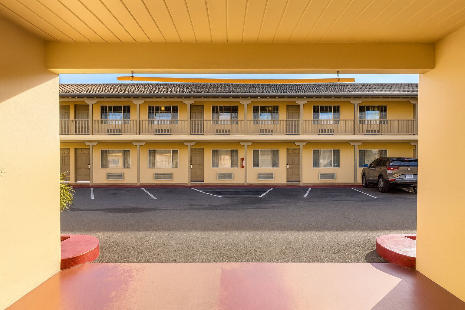 Et motel med en toetages bygning, en parkeringsplads og et rødt bord i forgrunden.