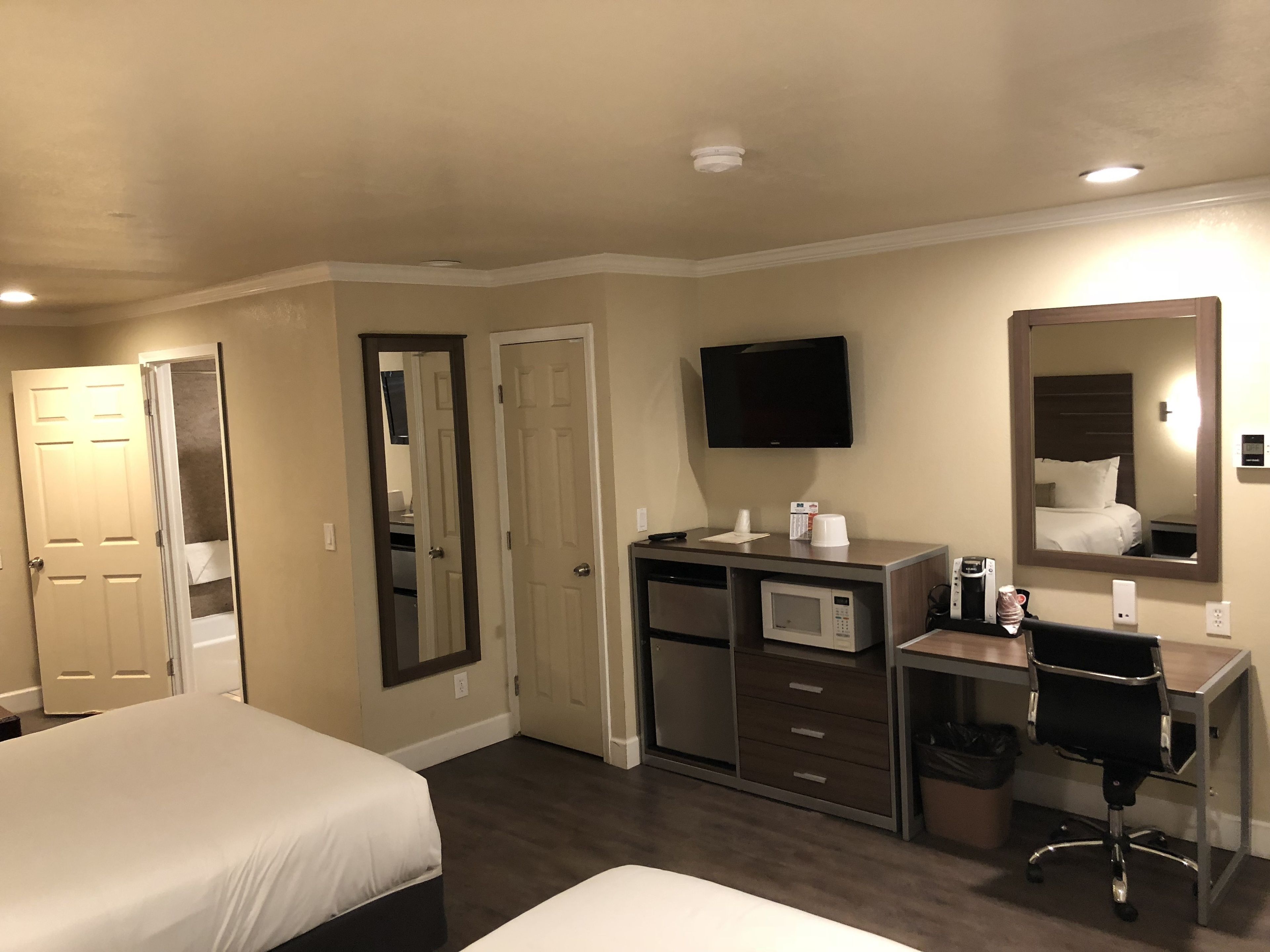A hotel room with two beds, a desk with a chair, a TV, a microwave, and a mirror.