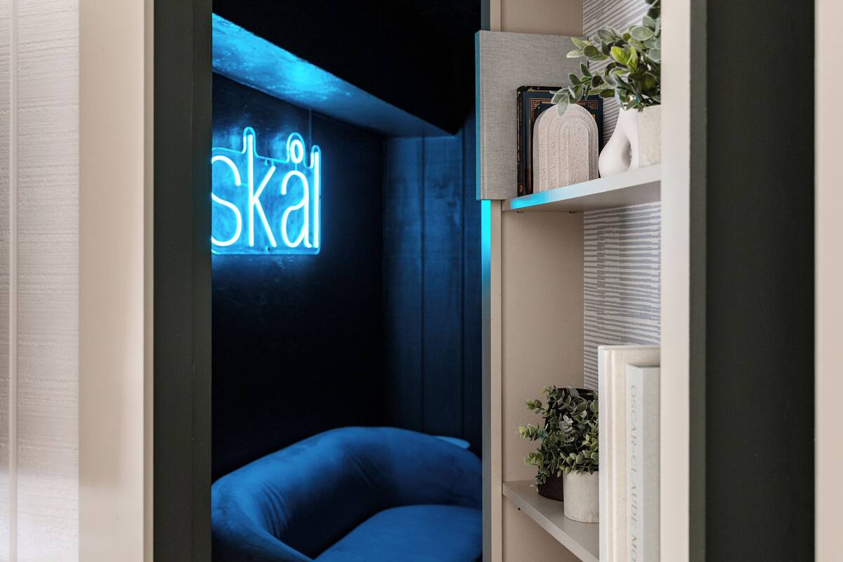Ein modernes Zimmer mit einer Neonreklame, einem blauen Sofa und einem Bücherregal.
