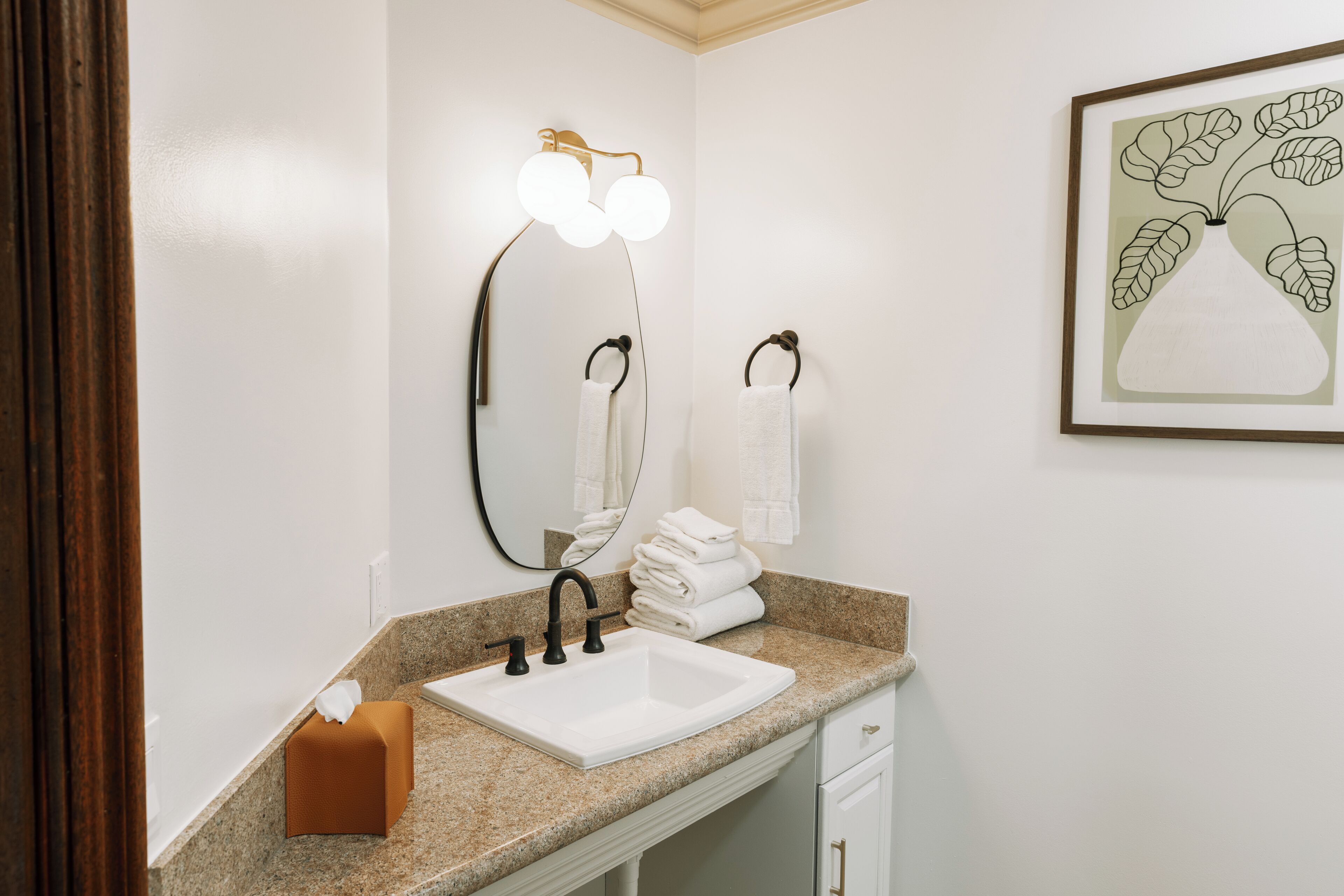 A bathroom with a white sink, a vanity mirror, and a framed artwork on the wall.